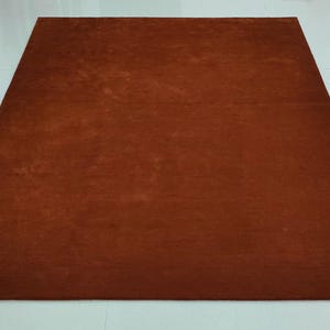 May include: A rectangular, solid brown rug. The rug is a single color and appears to be made of a soft material. The rug is placed on a white tiled floor. The rug is a home decor item.