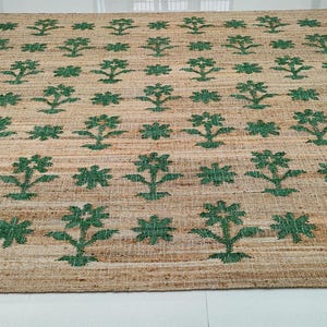 Op de afbeelding: Een vloerkleed van natuurlijke vezels met een geweven textuur en een herhalend patroon van groene bloemenmotieven.