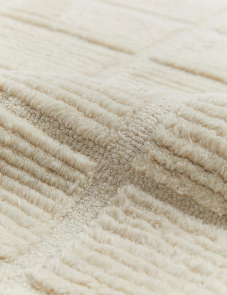 May include: Close-up of a cream-coloured rug with a textured, woven pattern. The rug has a soft, fluffy texture.