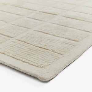 May include: A close-up of a cream-coloured rug with a textured, woven design. The rug has a subtle border around the edges.