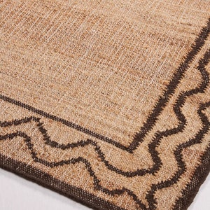 May include: A brown and beige jute rug with a dark brown wavy border.