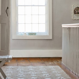 May include: A light brown rug with a white pattern in a room with a white painted wooden railing and a white door. The rug is on a wooden floor.