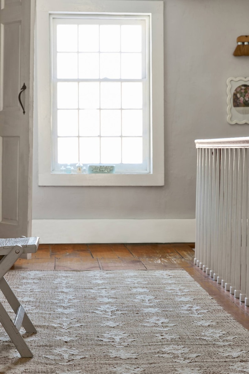 May include: A light brown rug with a white pattern in a room with a white painted wooden railing and a white door. The rug is on a wooden floor.