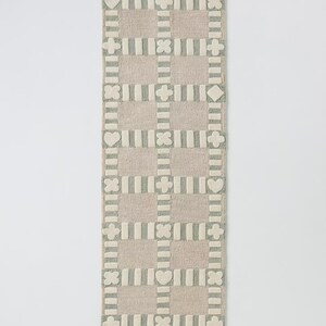 May include: A rectangular, patterned rug in a neutral color palette. The rug features a grid design with alternating squares of beige and gray, adorned with heart, diamond, and cross shapes. The rug is approximately 60 inches long.