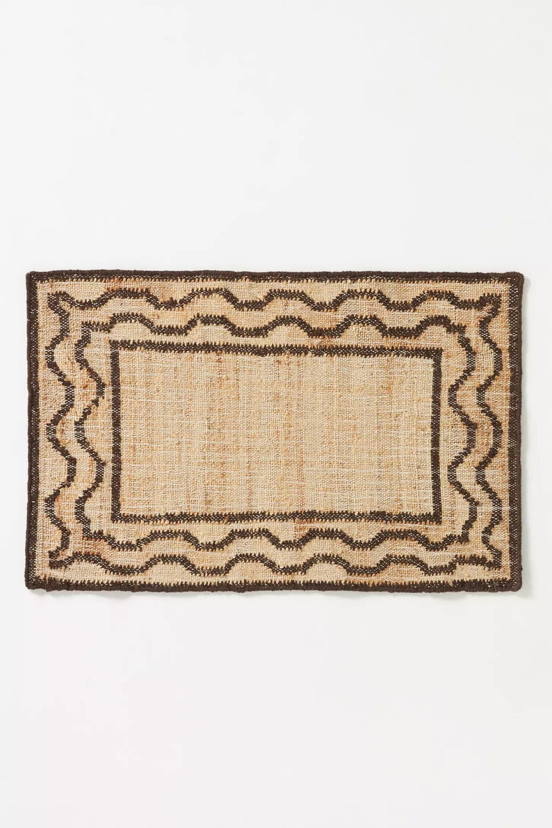 May include: A rectangular brown and beige jute rug with a wavy border design.