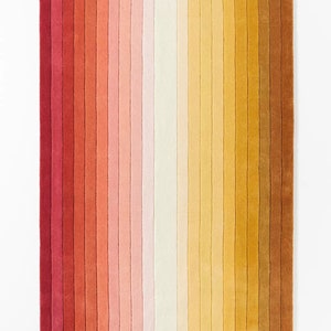 K&ouml;nnte beinhalten: Ein bunter gestreifter Teppich in Rot-, Orange-, Rosa-, Gelb- und Braunt&ouml;nen. Der Teppich ist aus weichem, pl&uuml;schigem Material gefertigt und hat ein modernes, geometrisches Design.