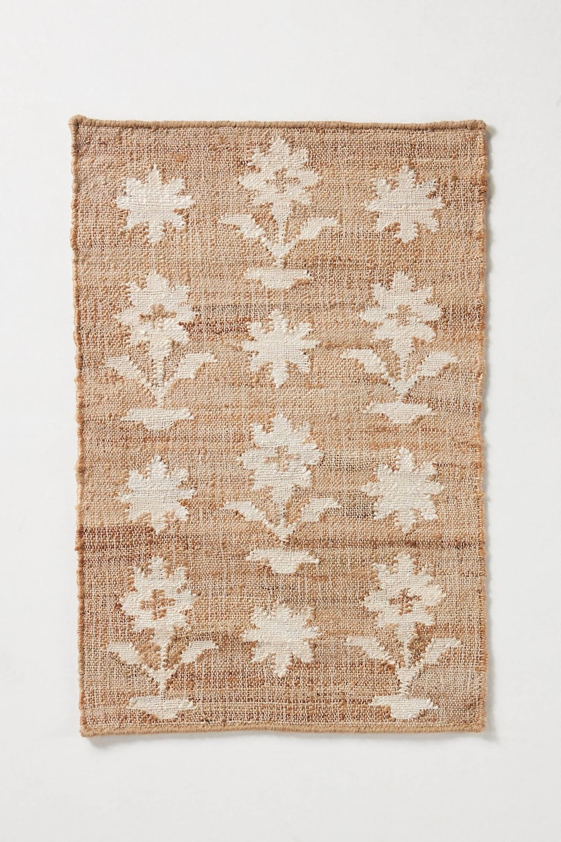 May include: A rectangular jute rug with a white floral pattern. The rug has a natural brown color and a woven texture.