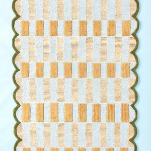 May include: A white and yellow checkered bath mat with a scalloped green border.