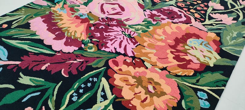 Puede incluir: Una alfombra negra con un patr&oacute;n floral con flores rosas, rojas y naranjas. Las flores son estilizadas y tienen una apariencia texturizada.