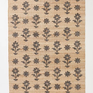 Pode incluir: Um tapete de fibra natural com um padr&atilde;o floral preto. O tapete tem uma textura tecida e uma forma retangular.