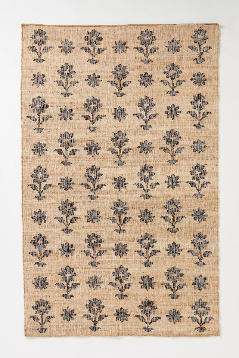 Pode incluir: Um tapete de fibra natural com um padr&atilde;o floral preto. O tapete tem uma textura tecida e uma forma retangular.
