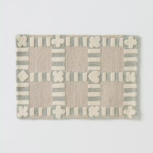 May include: Rectangular rug with a grid pattern. The rug features a light beige background with a border and grid lines in light gray. Decorative shapes like flowers and hearts are incorporated.