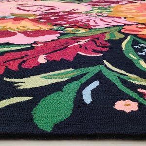 Puede incluir: Una alfombra negra con un estampado floral colorido. La alfombra presenta grandes flores rosas, rojas, amarillas y azules con hojas verdes.