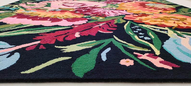 Puede incluir: Una alfombra negra con un estampado floral colorido. La alfombra presenta grandes flores rosas, rojas, amarillas y azules con hojas verdes.