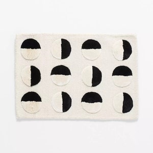 May include: A white bath mat with a black and white geometric pattern of half circles. The circles are arranged in three rows of four.