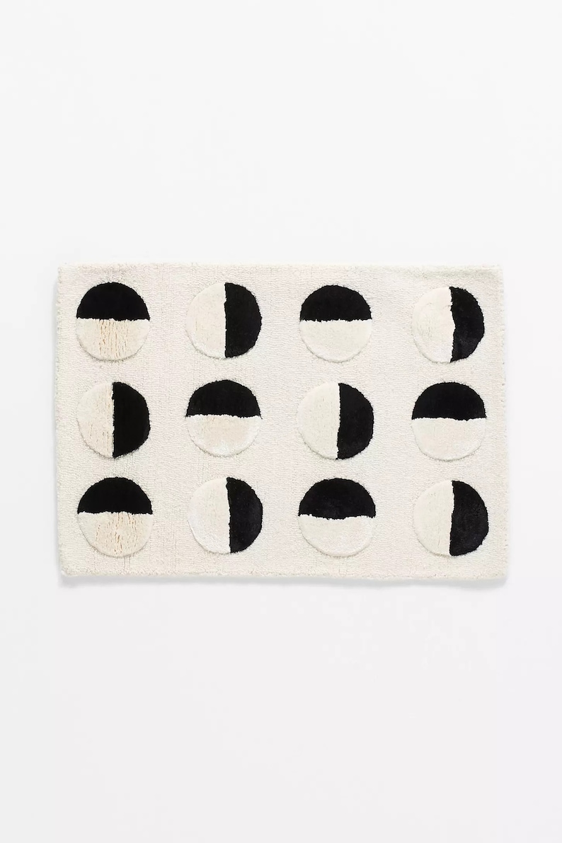 May include: A white bath mat with a black and white geometric pattern of half circles. The circles are arranged in three rows of four.