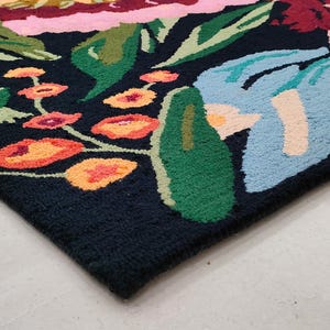 Puede incluir: Una alfombra negra con un estampado floral colorido. La alfombra presenta grandes flores azules, rosas y verdes con acentos amarillos y naranjas.