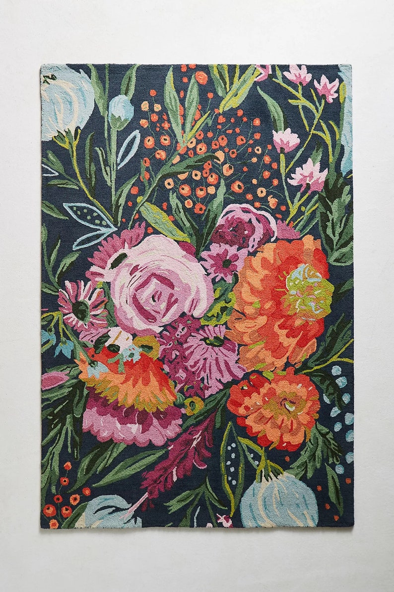 Puede incluir: Una alfombra azul marino con un patr&oacute;n floral con flores rosas, naranjas y verdes. La alfombra tiene un aspecto y una sensaci&oacute;n de tejido a mano.