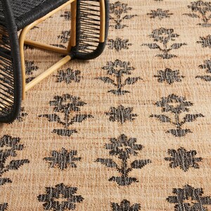 Pode incluir: Um tapete de fibra natural com um padr&atilde;o floral preto. O tapete &eacute; tecido com uma superf&iacute;cie texturizada, ligeiramente &aacute;spera.