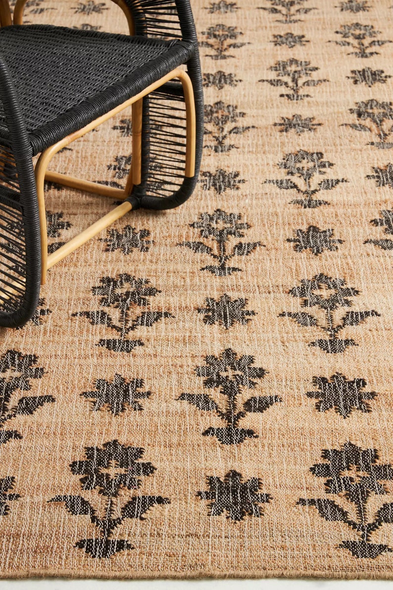 Pode incluir: Um tapete de fibra natural com um padr&atilde;o floral preto. O tapete &eacute; tecido com uma superf&iacute;cie texturizada, ligeiramente &aacute;spera.