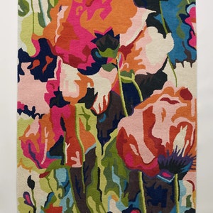 Puede incluir: Una alfombra colorida con un diseño floral que presenta grandes flores rosas, naranjas y rojas sobre un fondo azul oscuro.