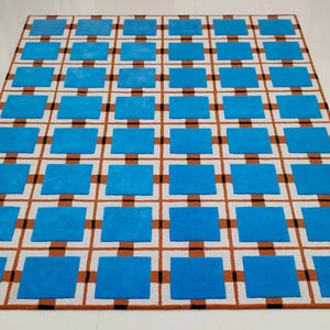 May include: A rectangular rug with a geometric pattern. The rug features a grid design with alternating blue squares and brown and black lines on a white background. The rug is made of a soft material.