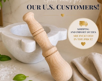May include: A white marble mortar and pestle set featuring a smooth, light-colored wooden pestle resting against the bowl. The mortar has a rounded shape with four small protruding tabs around the rim, accompanied by fresh green basil leaves and salt.
