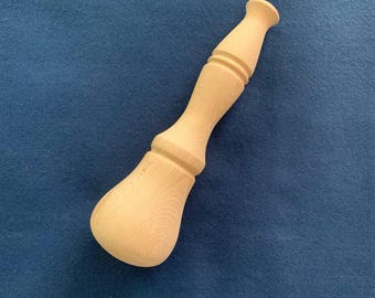 May include: A light-colored, unfinished wooden pestle with a bulbous base and a flared top. The pestle has a turned design with two distinct rings near the center. The wood grain is visible, and the object is set against a blue background.
