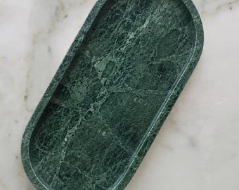 May include: An oval-shaped tray crafted from dark green marble with natural white veining throughout. The tray features a smooth, polished surface and a raised rim, providing a shallow basin for holding small items on a flat surface.