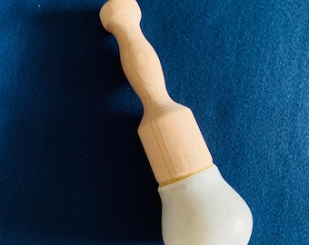 May include: A light-colored wooden massage tool with a rounded handle and a white, bulbous head. The tool is designed for therapeutic use and is shown against a blue background.