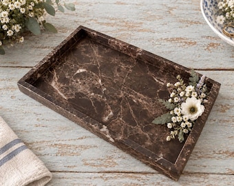 May include: A rectangular dark brown marble tray with white veining, featuring a decorative arrangement of small white flowers, lavender sprigs, and green fern leaves attached to the right side of the tray's interior surface.