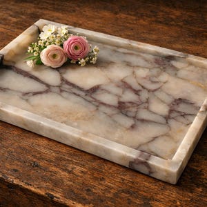 May include: A rectangular marble tray with a cream and burgundy veined pattern. The tray has a raised edge and is decorated with a small arrangement of pink and white flowers. The tray is displayed on a dark wood surface.