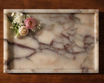 May include: Rectangular marble tray with a cream and burgundy veined pattern. A small arrangement of white and pink flowers rests on the tray's edge. The tray is a decorative item, suitable for serving or display.