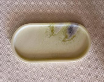 May include: An oval-shaped tray with a smooth, polished surface. The tray features a pale, creamy yellow base color with marbled accents of light green and a small patch of dark purple, creating a natural, stone-like appearance with raised edges.