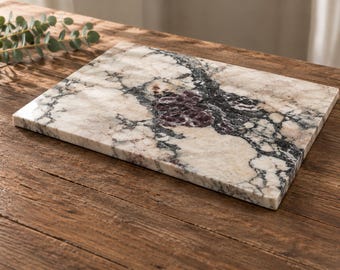 May include: A rectangular marble serving board featuring a polished surface with a complex pattern of cream, white, dark grey, and black veining, accented by a central cluster of deep purple mineral inclusions across the flat stone slab.