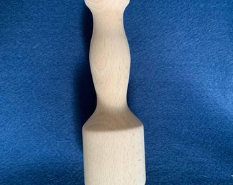 May include: A light-colored wooden muddler with a rounded top and a cylindrical base. The handle has a curved, ergonomic design. The muddler is made of natural wood and is set against a blue background. This kitchen tool is used for mixing ingredients in cocktails.