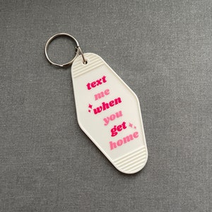 May include: White motel key chain with a pink and red text that reads "text me when you get home".