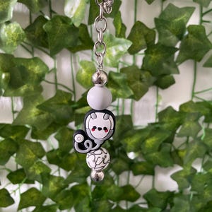 May include: A black and white cartoon character keychain with a stethoscope. The character has red cheeks and a white body with black outlines. The keychain is attached to a silver chain and a silver ring.