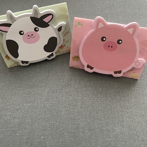 May include: Two colorful animal-shaped sticky notes. A black and white cow sticky note and a pink pig sticky note.