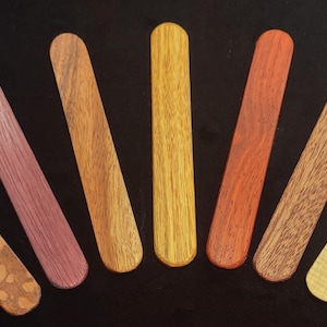 May include: A set of nine wooden sticks, each with a different wood grain and color. The sticks are arranged in a semi-circle, with the darkest stick at the top and the lightest stick at the bottom.