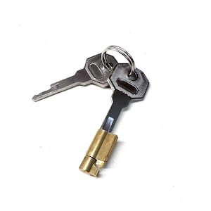 Könnte beinhalten: Zwei silberne Schlüssel mit einem Messingverschluss, der an einem silbernen Ring befestigt ist. Die Schlüssel haben eine silberne Oberfläche und sind an einem Messingverschluss befestigt.