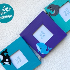 May include: Three turquoise and purple picture frames with felt animal appliques. The frames are labeled "fein & flizig".