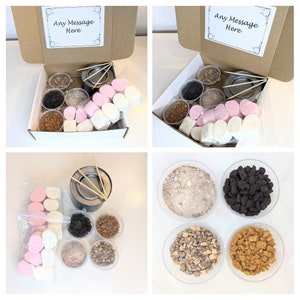 May include: A white box with a brown lid containing a s'mores kit. The kit includes marshmallows, chocolate, graham crackers, and skewers. The box has a label that says "Any Message Here".