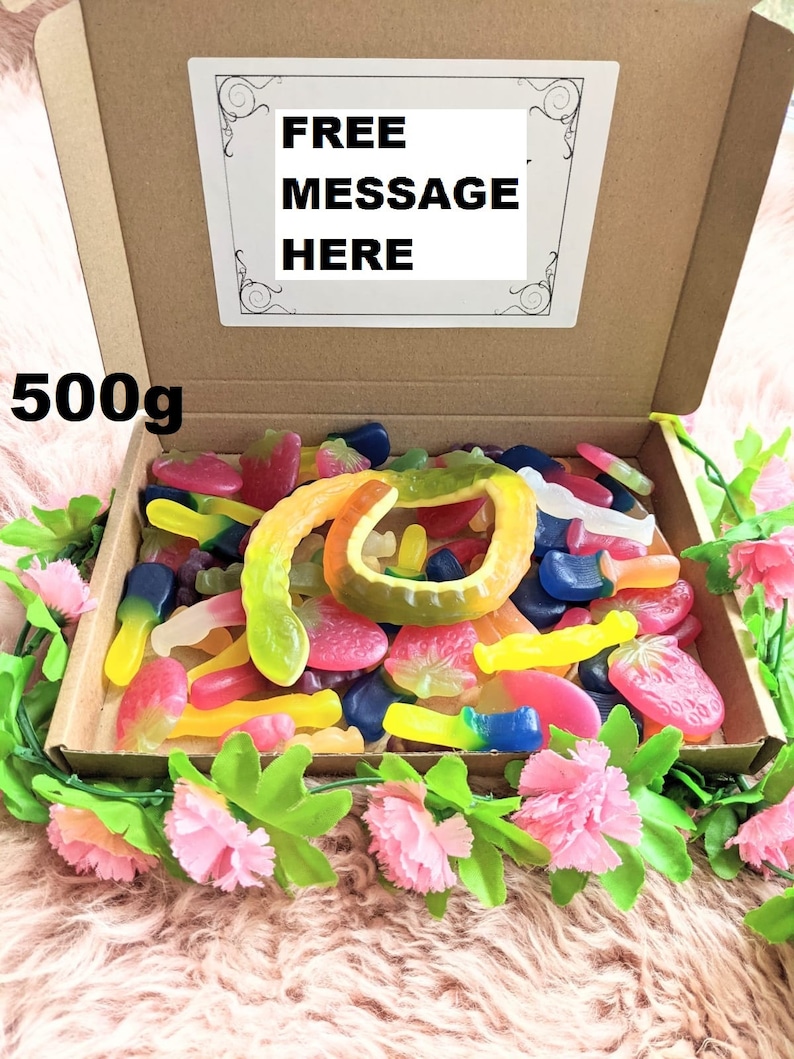 May include: A brown cardboard box filled with colourful gummy sweets, including worms, strawberries, and other shapes. The box is open and the sweets are visible. The box is labelled "500g" and has a white label with the text "FREE MESSAGE HERE".