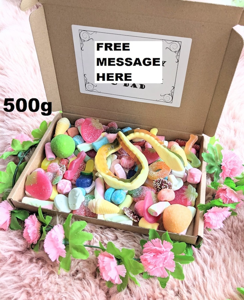 May include: A cardboard box filled with a variety of colourful sweets, including gummy worms, jelly beans, and marshmallows. The box is labelled "FREE MESSAGE HERE" and "500g".
