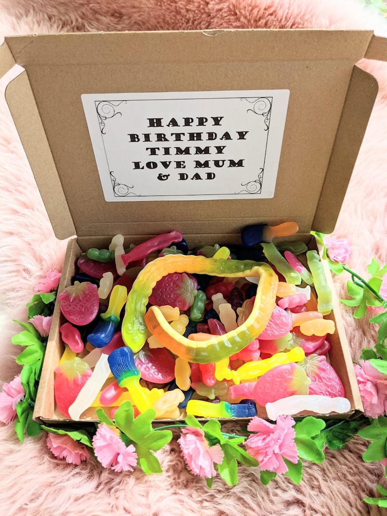 May include: A cardboard box filled with colourful gummy sweets, including gummy worms, gummy strawberries, and gummy fish. The box has a white card on top with the text "Happy Birthday Timmy Love Mum & Dad".
