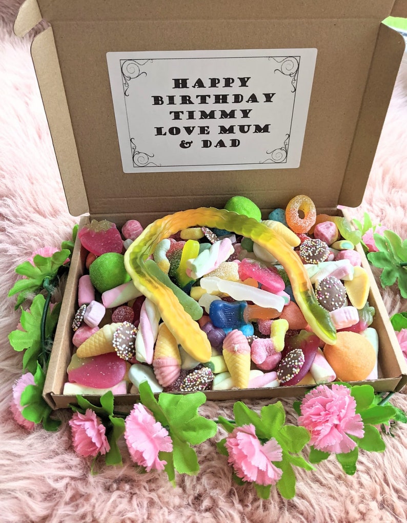 May include: A brown cardboard box filled with colourful sweets, including gummy bears, marshmallows, and lollipops. The box has a white card on top with the text "Happy Birthday Timmy Love Mum & Dad".