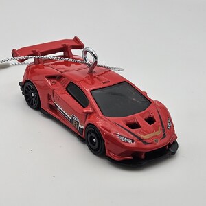May include: A red Lamborghini race car ornament with a black and gold stripe and a silver hook for hanging.