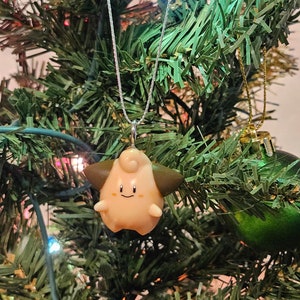 May include: A pink and brown Pokemon character ornament hanging from a silver chain on a green Christmas tree.