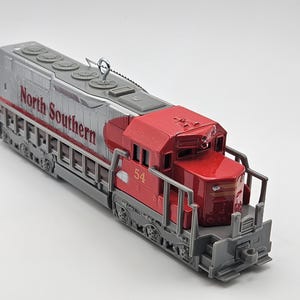 May include: A model train locomotive with a red and silver color scheme. The words "North Southern" are printed on the side. The number "54" is visible on the front of the red cab. The train has detailed features.